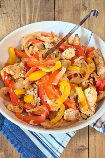 Chicken Fajitas with yellow and red bell peppers and onions in a white bowl with a blue and grey cloth underneath the bowl