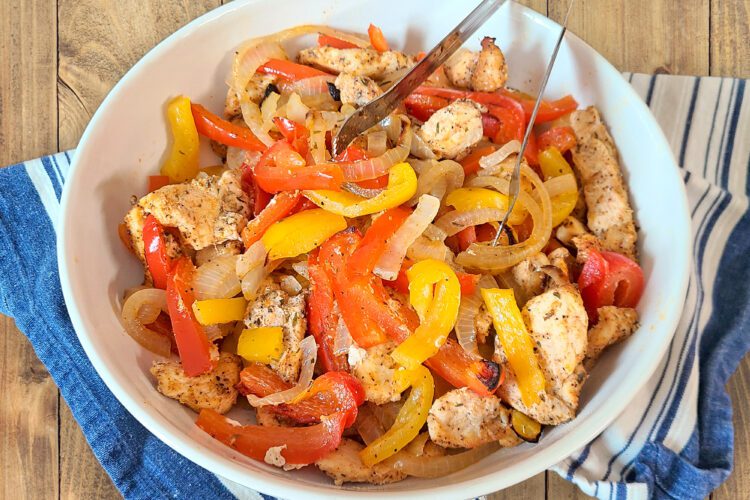 Chicken Fajitas with yellow and red bell peppers and onions in a white bowl with a blue and grey cloth underneath the bowl