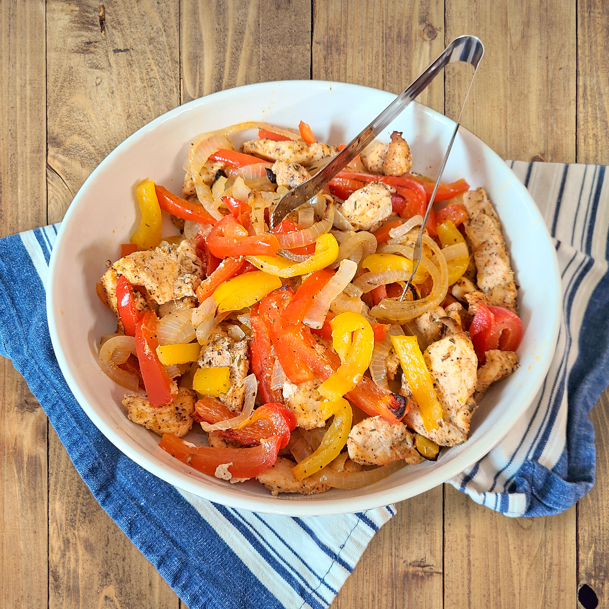 Chicken Fajitas with yellow and red bell peppers and onions in a white bowl with a blue and grey cloth underneath the bowl