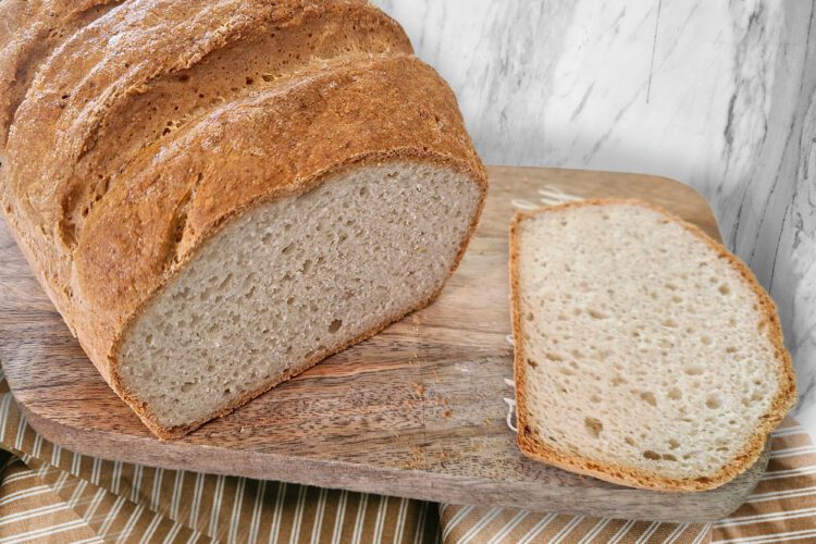 A gluten free loaf of bread sitting on a cutting board with one slice sliced off