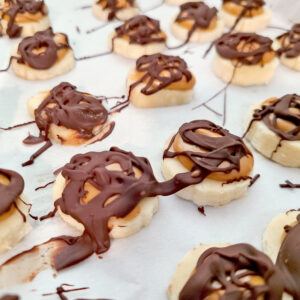 Chocolate drizzled on top of peanut butter topped frozen bananas